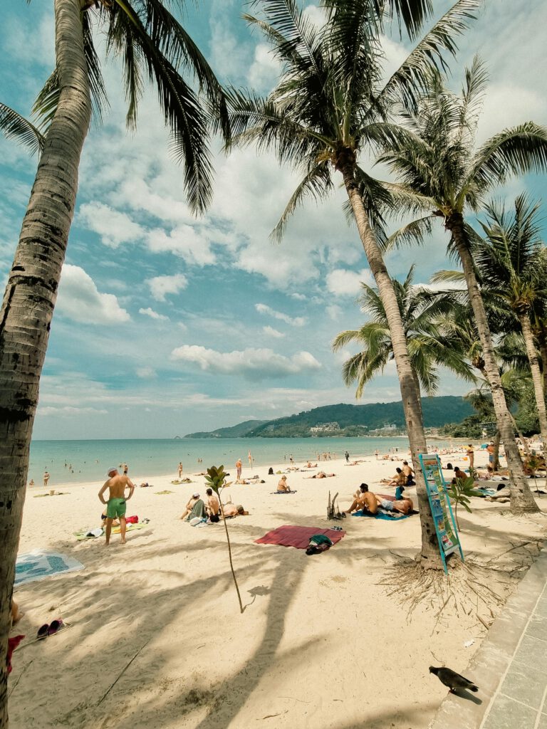 pexels-photo-15917114-15917114 Sunny day at Patong Beach, Phuket, Thailand, featuring palm trees, sand, and relaxing tourists.